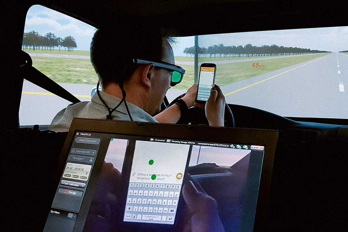 Driver in a simulator wearing eye-tracking, attention divided between road and in-vehicle interface